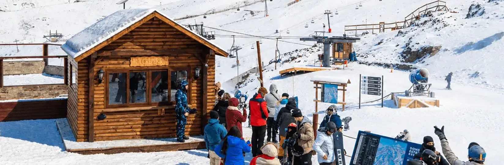 Cabana de madeira da La Creperie na neve, com fila de esquiadores esperando.