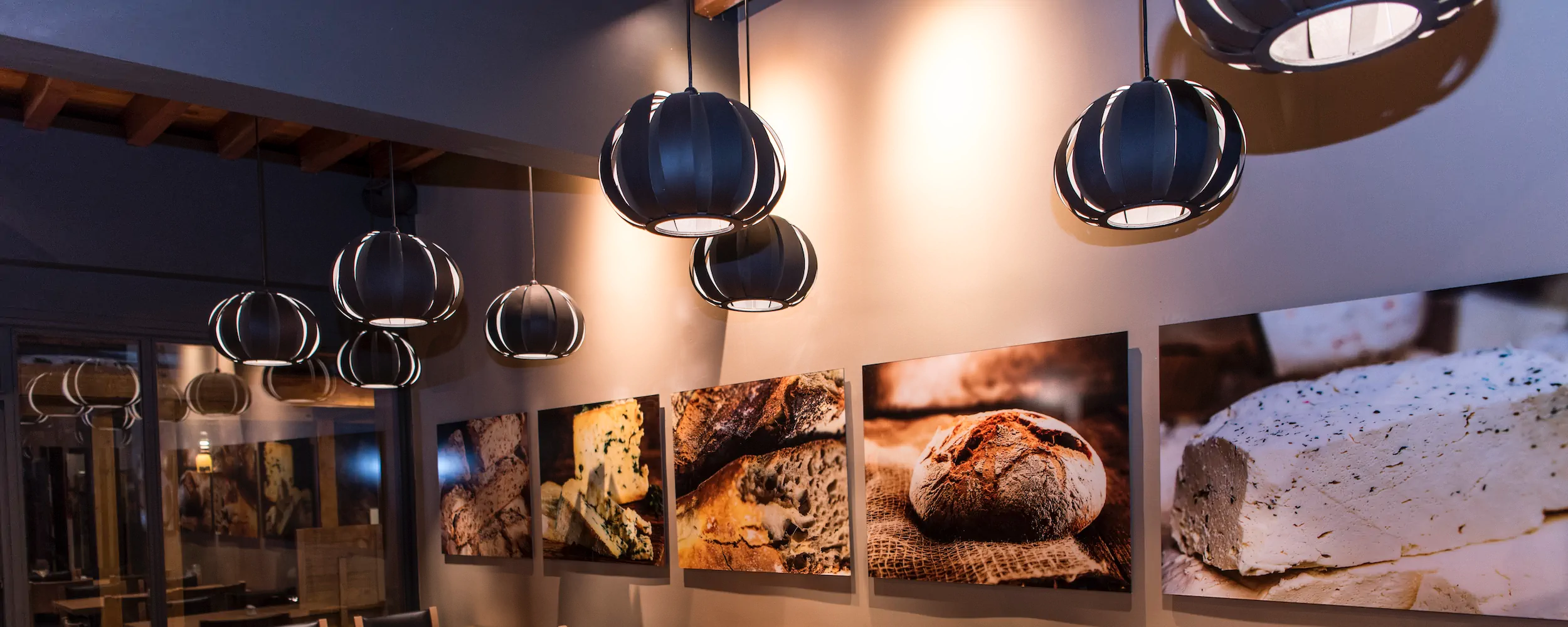 Interior do Monte Bianco, com luminárias pendentes e fotos de queijos e pães artesanais na parede.