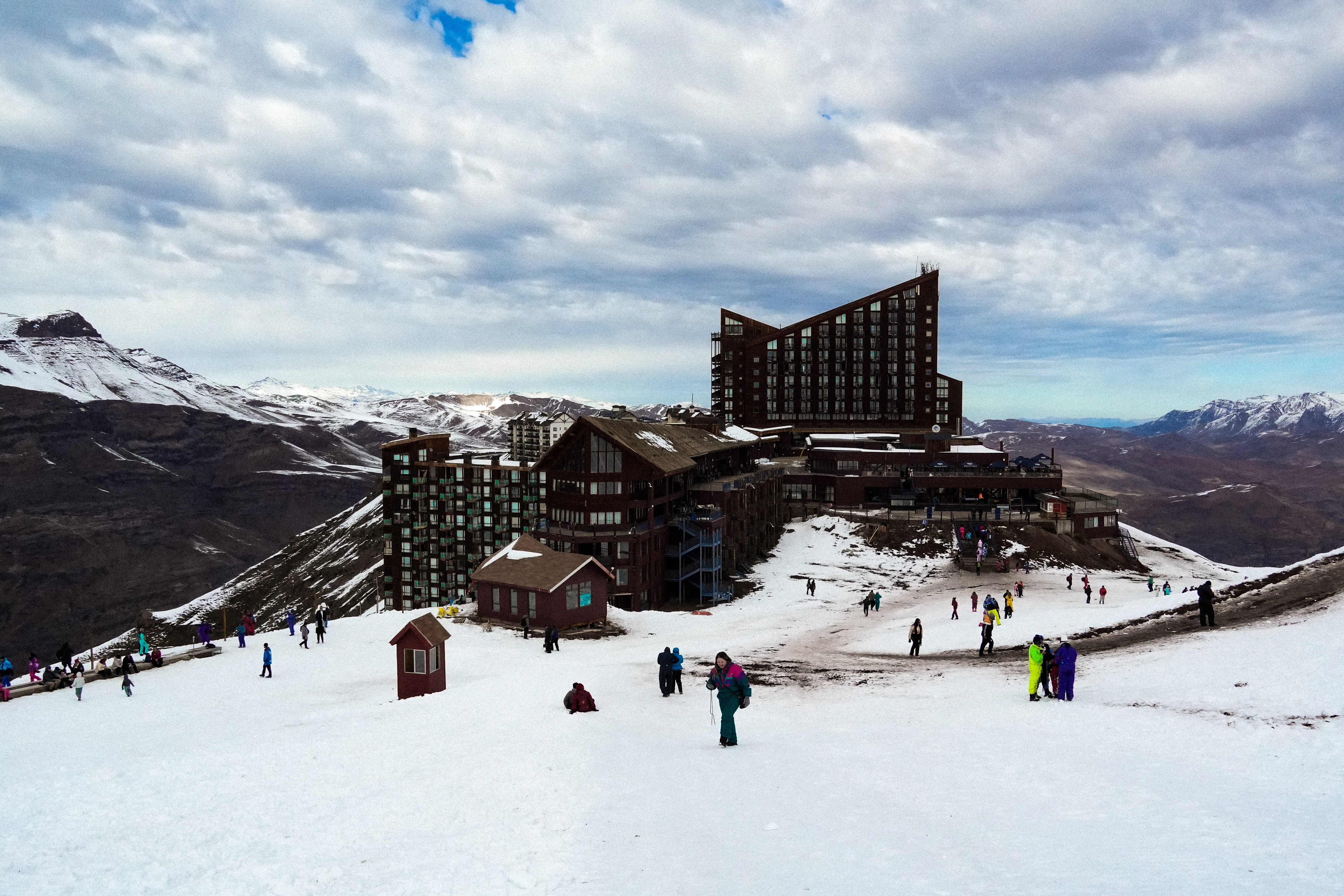 A base do Valle Nevado num dia de inverno, com viajantes circulando entre os hotéis e a neve.