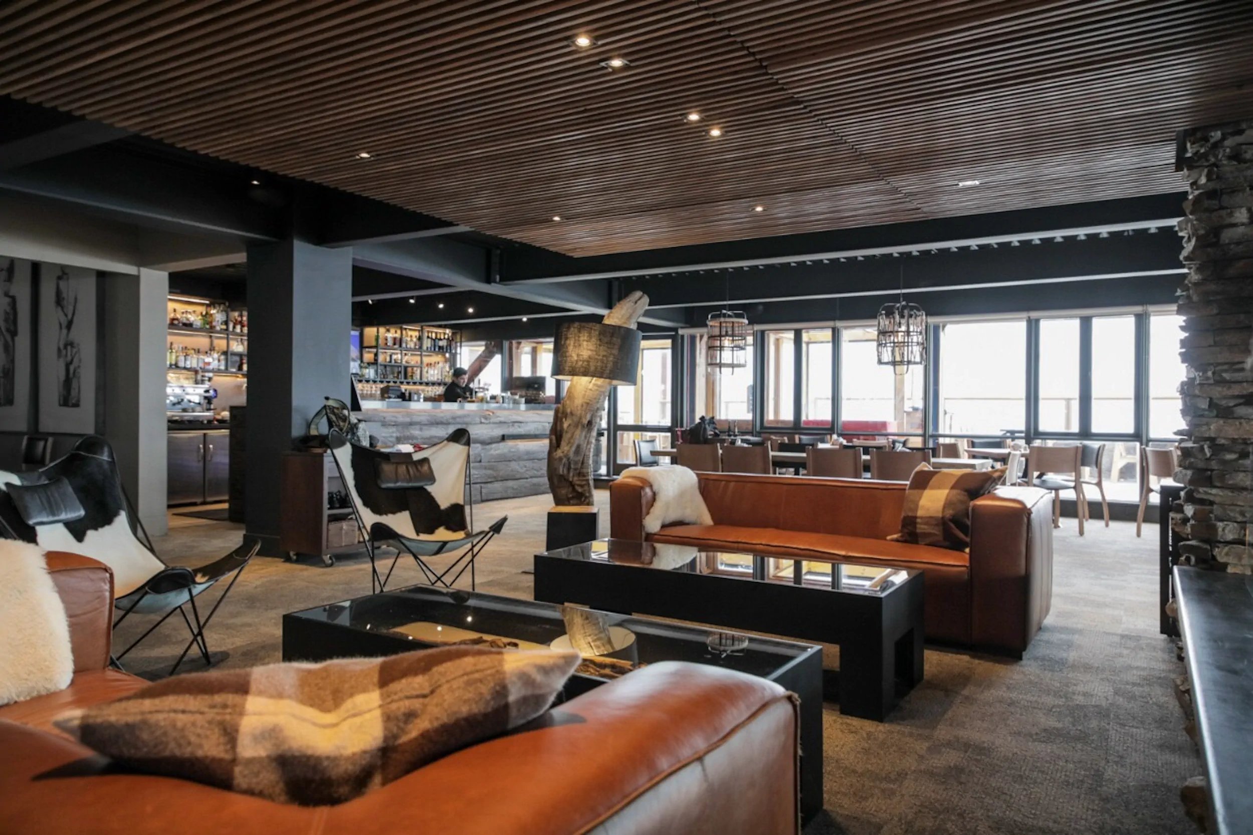 Salão do Valle Lounge, com sofás de couro, lareira e janelas amplas para a montanha.