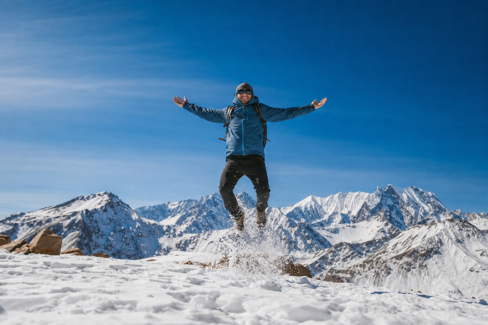 Viajante saltando de braços abertos diante dos picos nevados.
