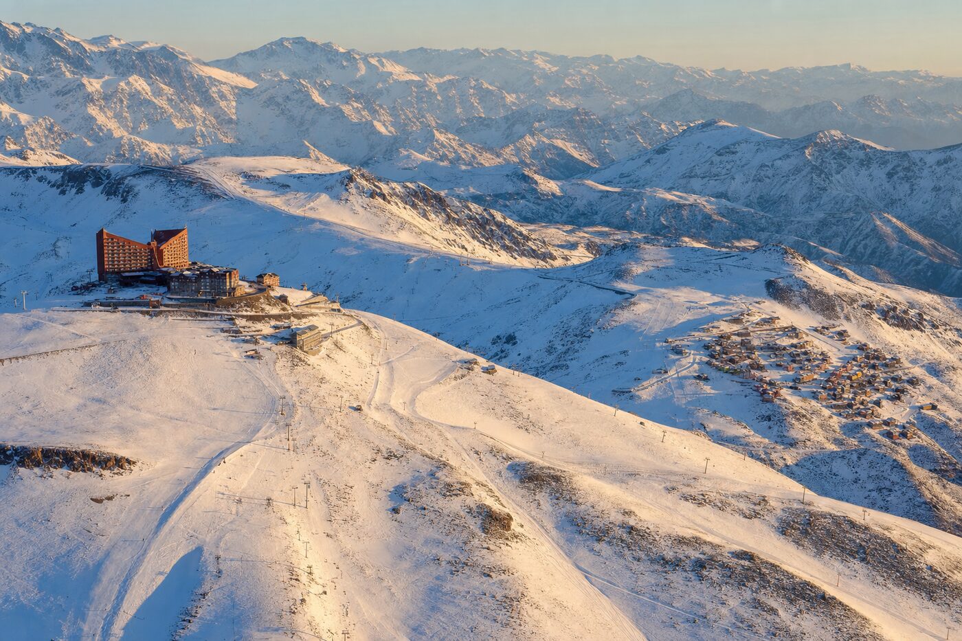 Vista aérea de Valle Nevado e La Parva interligadas no inverno, com os vales nevados e as pistas conectadas.